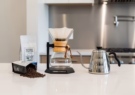 The Chemex Ottomatic 2.0 coffee maker sitting elegantly on a modern kitchen counter next to a bag of coffee beans.