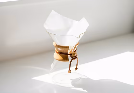 A classic glass Chemex coffee maker with a white paper filter perfectly placed inside, ready for brewing.