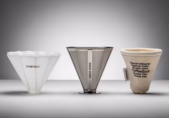Three types of filters for a Chemex displayed side-by-side: a paper filter, a metal Kone filter, and a cloth CoffeeSock filter.