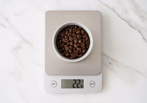 A digital kitchen scale showing a reading of 22 grams with whole coffee beans in a small bowl on top.