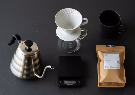 A complete pour-over coffee brewing setup including a ceramic V60, a gooseneck kettle, a digital scale, and a coffee mug.
