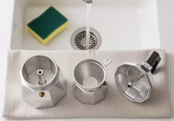 The three main parts of a moka pot—boiler, filter funnel, and collection chamber—disassembled and laid out on a cloth for cleaning.