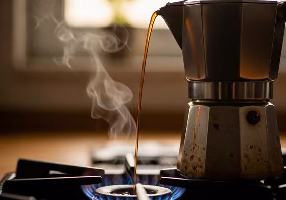 Close-up shot of a Pezzetti moka pot on a gas stove, with rich, dark coffee streaming into the upper chamber.