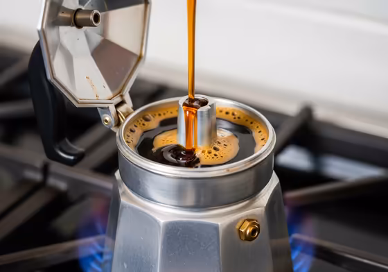 A moka pot on a stove with a slow, steady, rich stream of coffee flowing from the spout, demonstrating a successful brew.