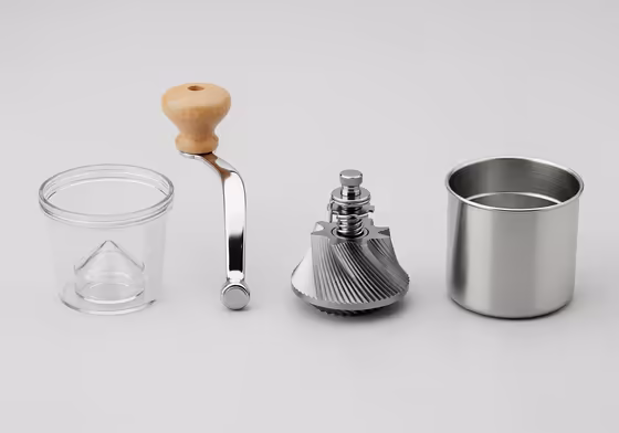 An exploded view of a manual coffee grinder showing its parts: hopper, handle, burrs, and grounds chamber.