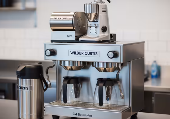 An integrated Wilbur Curtis coffee brewing system, showing the grinder docked directly on top of the batch brewer.