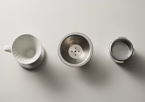 A collection of different coffee filter baskets including a cone-shaped drip filter, a flat-bottom drip filter, and a metal espresso portafilter basket.